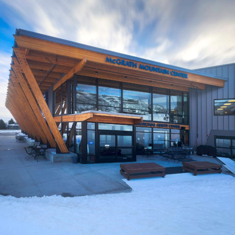 Image of the Mountain Center Building. It is an angled building with floor to ceiling glass windows. The building stands above the snow.